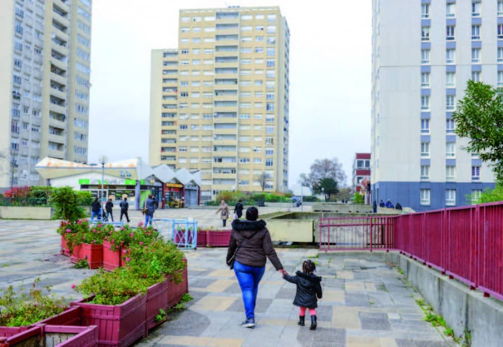 L'image montre des personnes marchant sur une dalle entre des immeubles