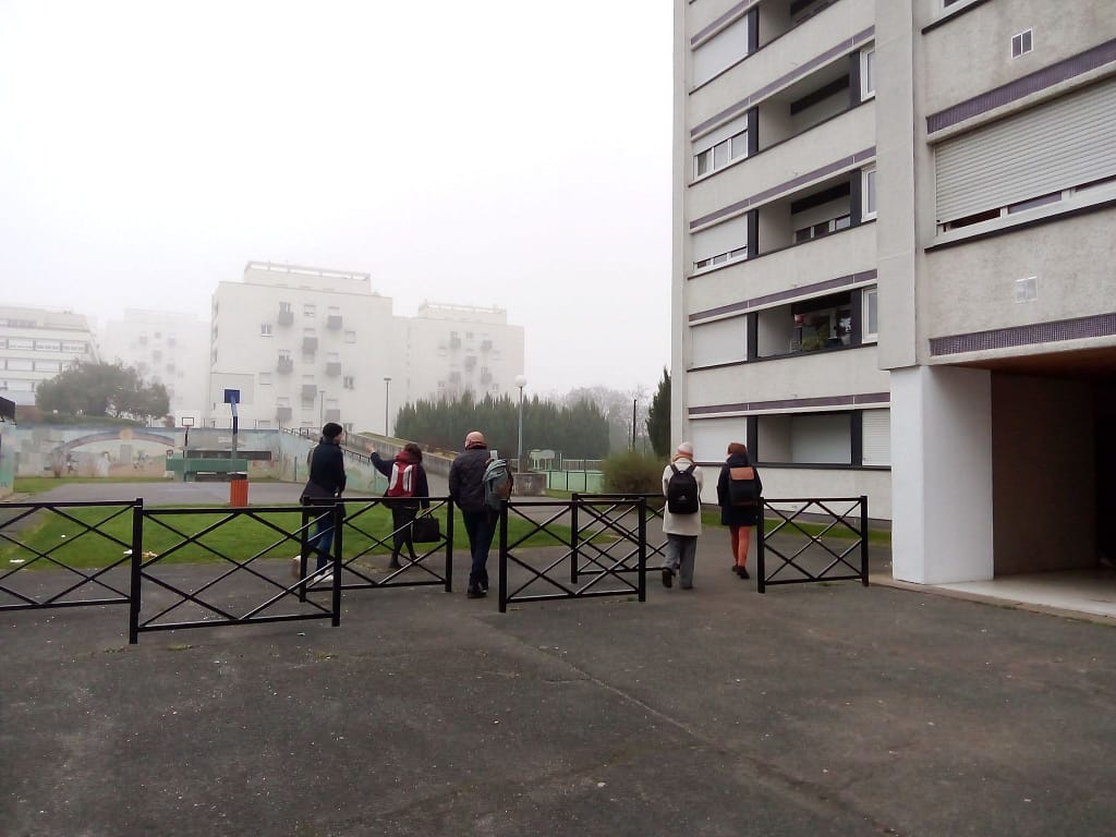 L'image montre 4 personnes marchant sur un parvis de tours, dans le brouillard.