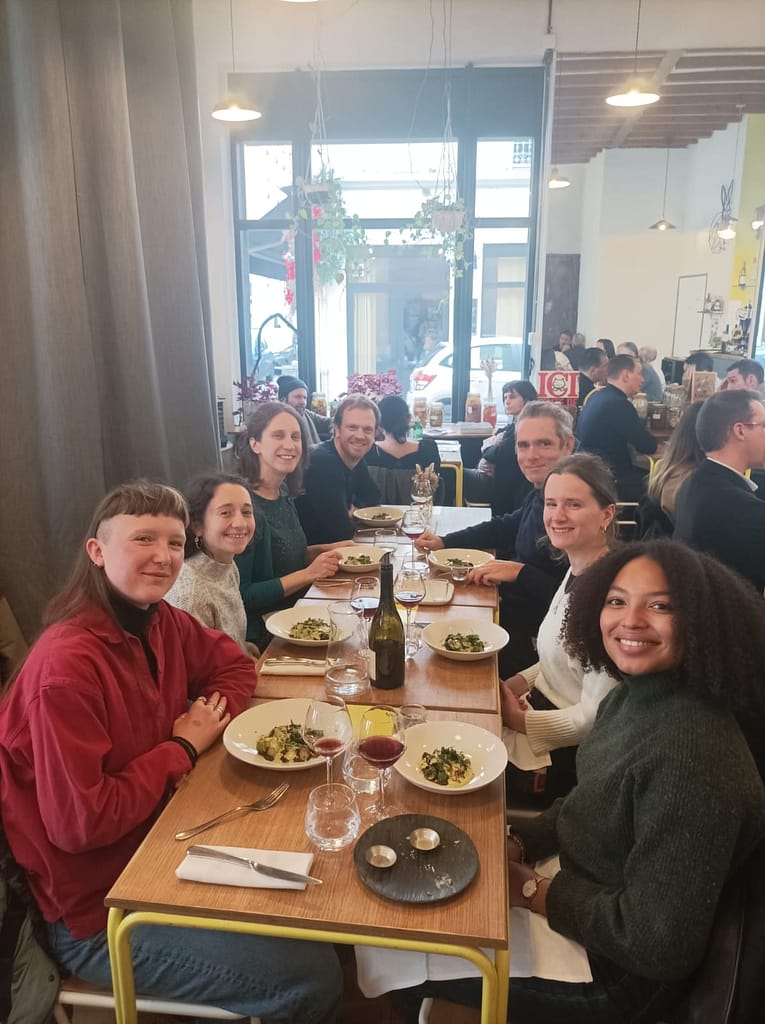 l'image montre 6 personnes souriantes assises autour d'une table au restaurant, elles regardent la caméra