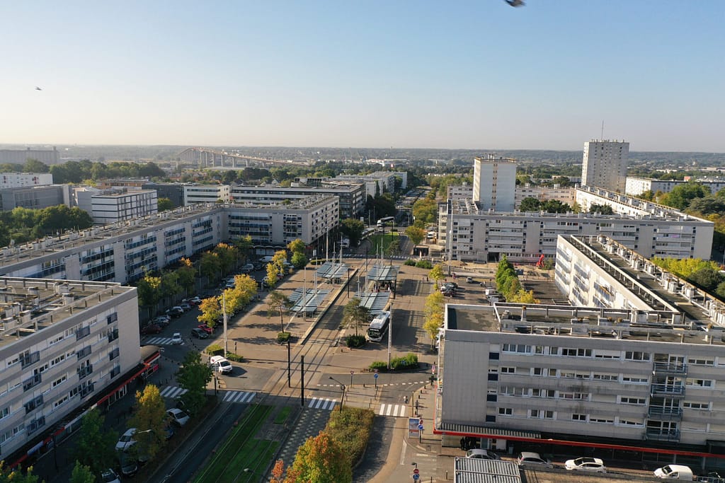 L'image montre la ville de saint herblain vue depuis le ciel : on voit un grand boulevard arboré, brodé d'immeubles de 4 étages blancs et éparses