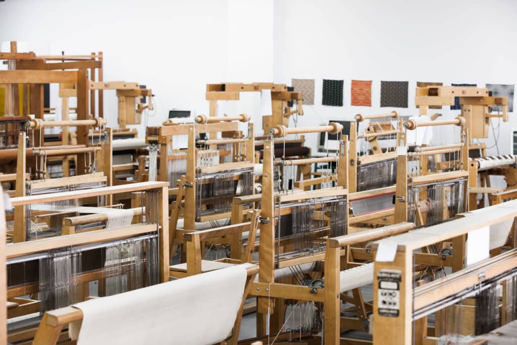 L'image montre une salle avec des métiers à tisser en bois qui la remplisse