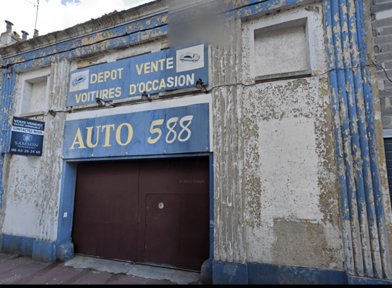 L'image montre la devanture d'un ancien garage, de couleur bleue. texte : "dépot vente voitures d'ocasion, auto 588"