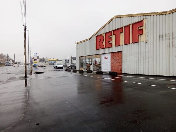 L'image montre un parking de supermarché sous la pluie, enseigne rETIF