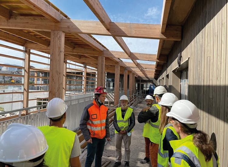 L'image montre des personnes avec des casques de chantier et des gileys jaunes de sécurité sur un chantier d'un bâtiment avec poutres apparentes