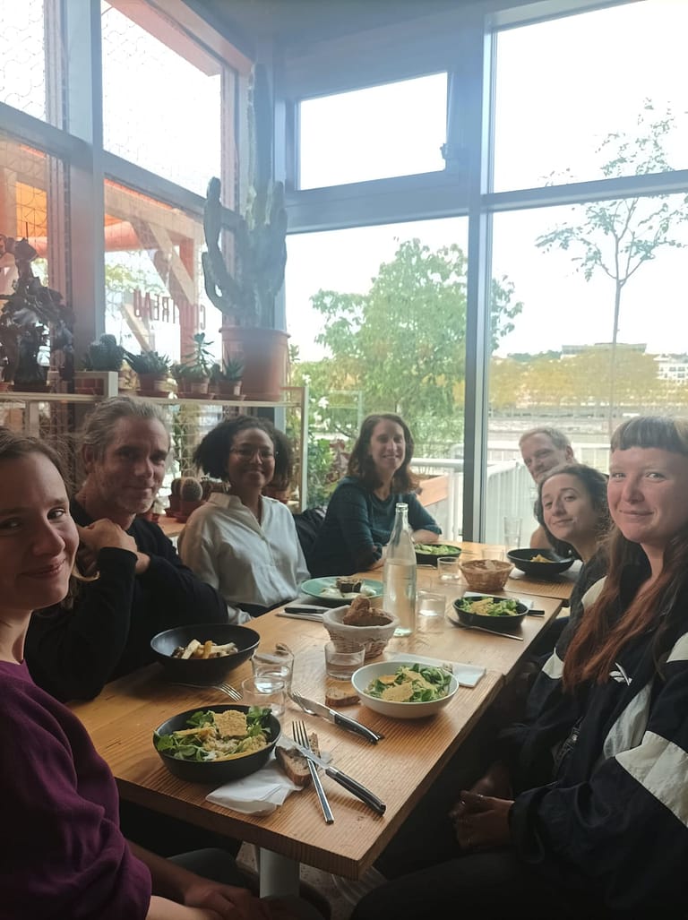 L'image montre 6 personnes autour d'une table qui regardent l'objectif, dans un restaurant lumineux