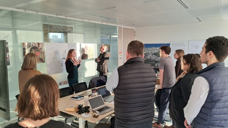 L'image montre 10 personnes debout autour d'une table devant des plans