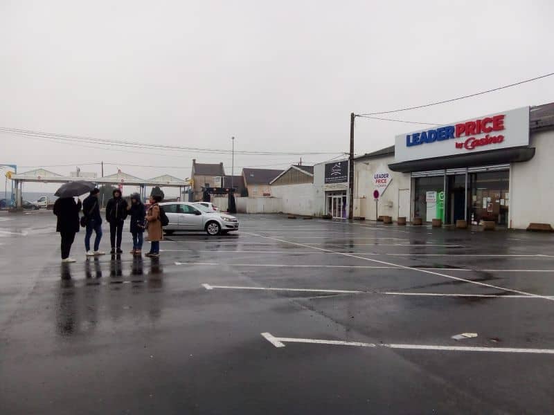 L'image montre 5 personnes avec des parapluies, regroupés sur le parking d'un centre commercial RETIF