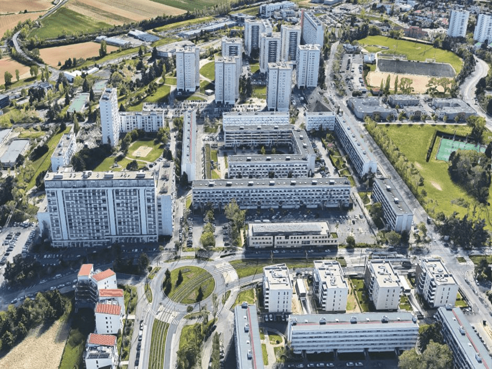 L'image montre le quartier des Minguettes à Lyon, composé de barres d'immeubles, de tours d'immeubles, entouré de champs