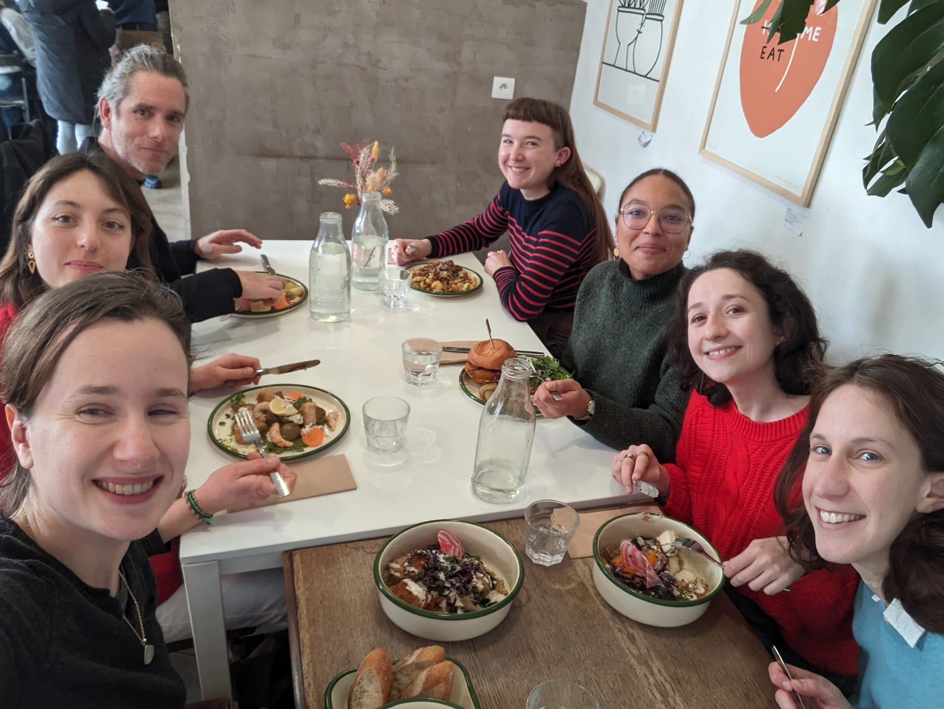 L'image montre 8 personnes assises autour d'une table dans un restaurant, qui soutient et regardent la caméra