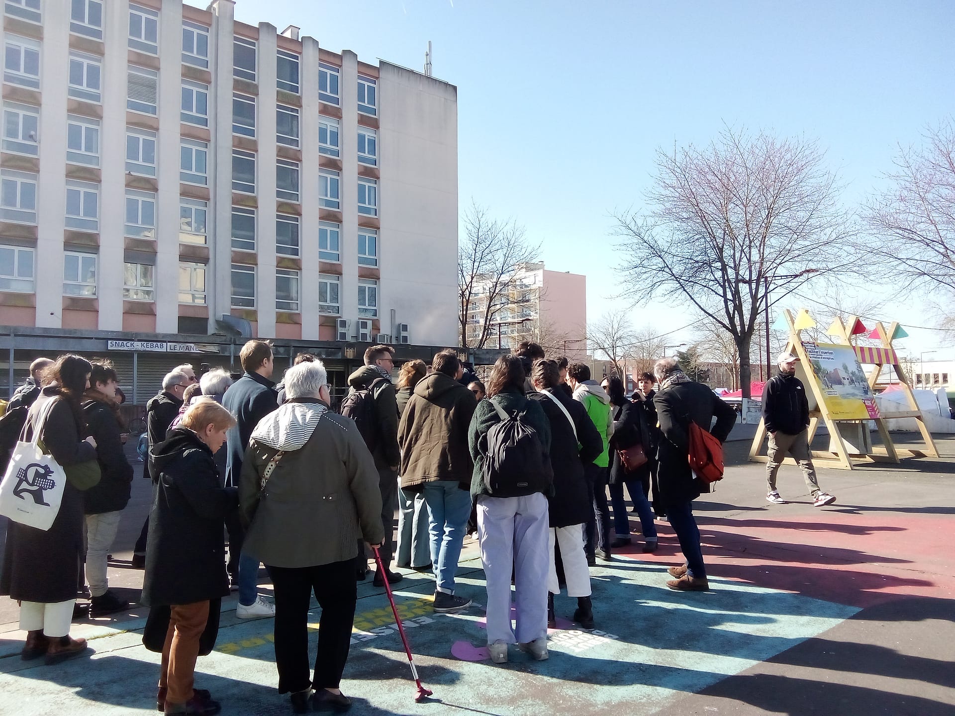 l'image montre un groupe d'une trentaine de personne à côté de barres d'immeubles, visitant le quartier